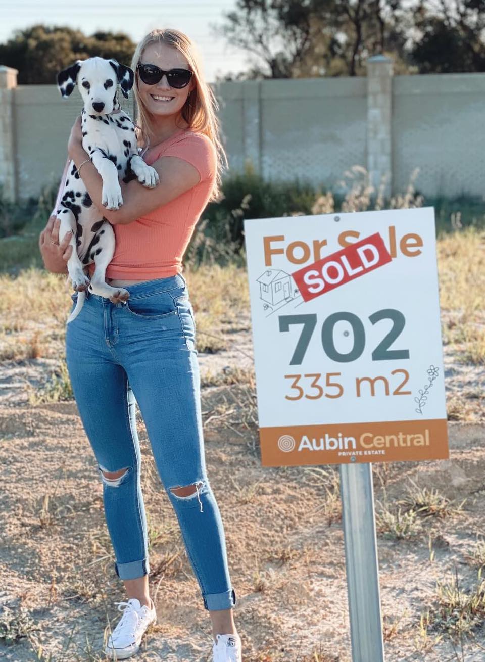 First home builder standing on their new land next to a sign that says "sold"