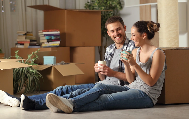 First home buyers sitting on the floor while unpacking and laughing.